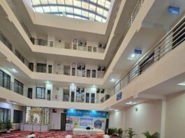 योग दिवस 2025 के अवसर पर बंद हॉल में सामूहिक योग करते वयस्क प्रतिभागी