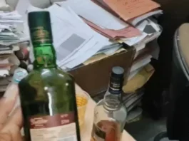 विश्वविद्यालय के कार्यालय में रखी शराब की दो बोतलें, पास में फैली हुई छात्रों की फाइलें और दस्तावेज।